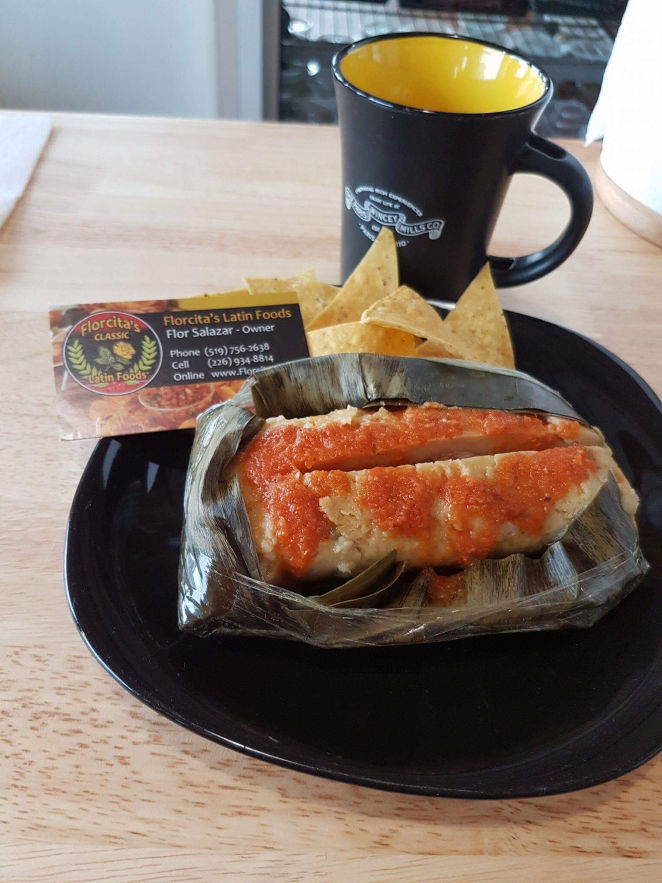 Hen tamales with Florcitas special sauce served on a plate with a cup in the background and business card.