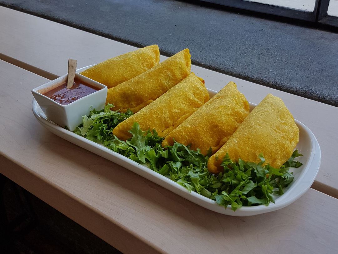 Four Columbian empanadas served on a plate with sauce.